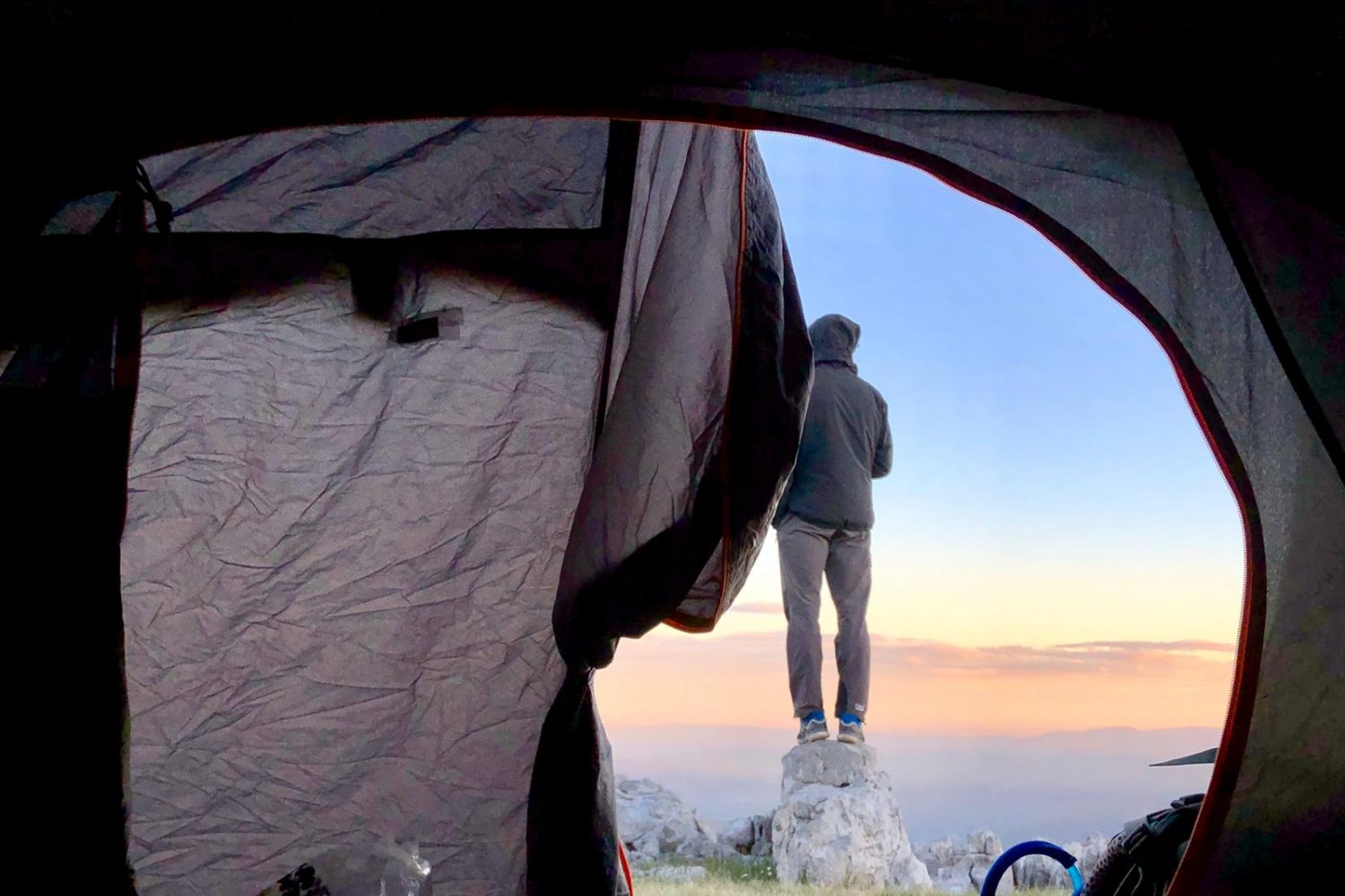 personne posant à l'aube face à un paysage panoramique, vue d'une tente